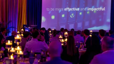 A group of people in a room lit dimly by candles in front of a screen displaying the text "to be more impactful and effective"