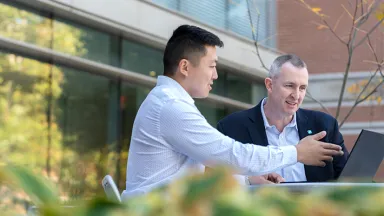 Two businessmen conversing and viewing a laptop screen outside