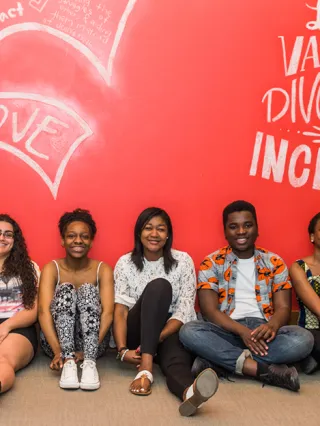 Eleven smiling students sitting in front of a red wall that reads "LeBow values diversity & inclusion"