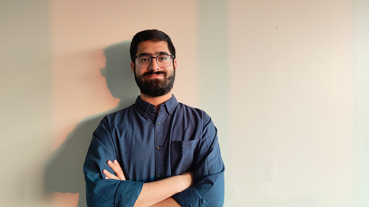Roshan stands against a light background, smiling with his arms crossed.