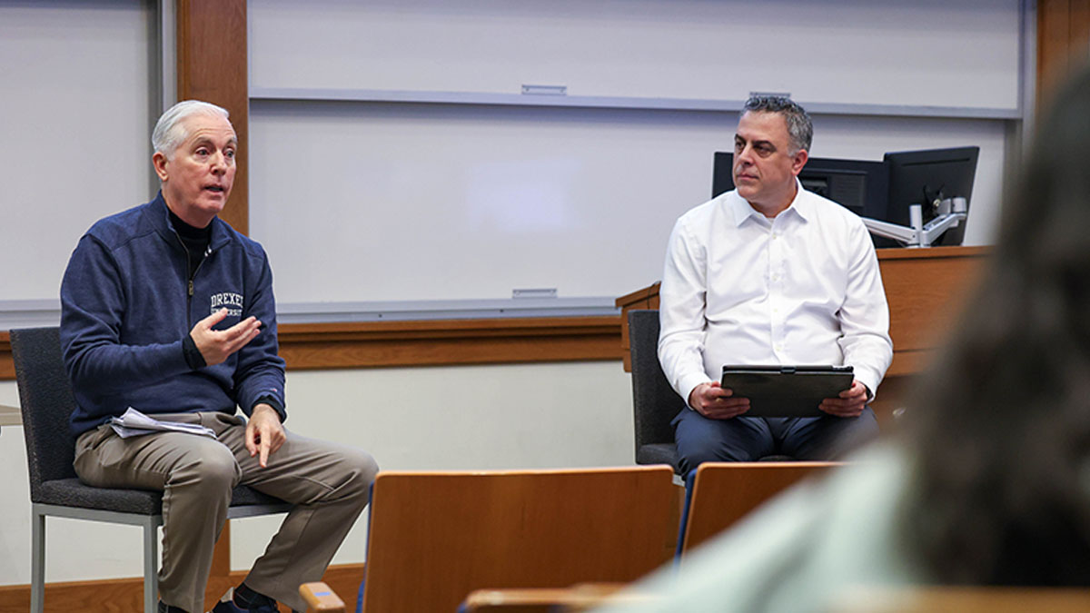 Two men seated at the front of a classroom
