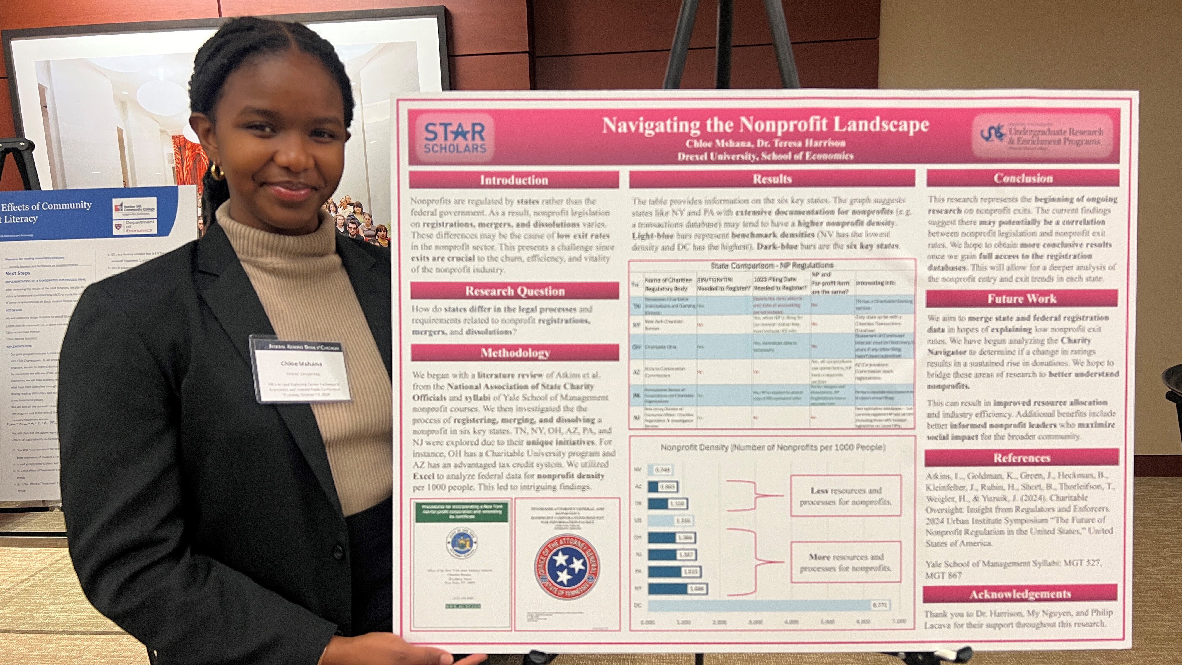 Chloe Mshana, BS economics '28, presenting her research A young woman in a black suit with a tan turtleneck sweater stands next to a horizontal poster with red headers and multiple charts visible