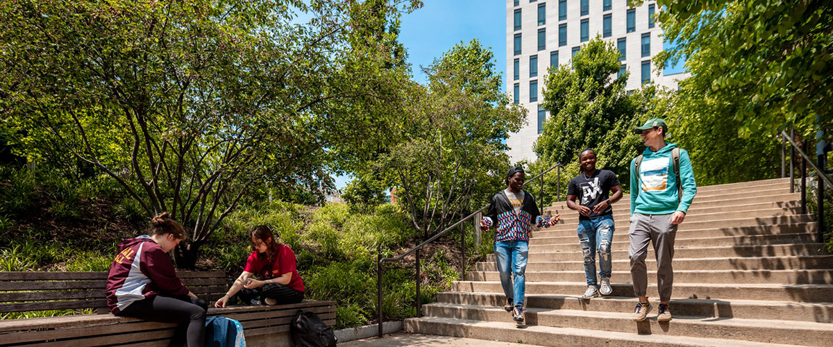 students walk through Drexel's campus on a sunny day, with Gerri C. LeBow Hall visible through the trees behind them