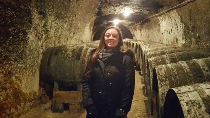 student standing in front of multiple aged wine barrells