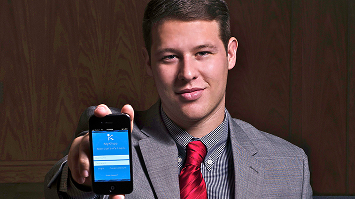 Skyler Logsdon holds up a smartphone with his app open on the screen