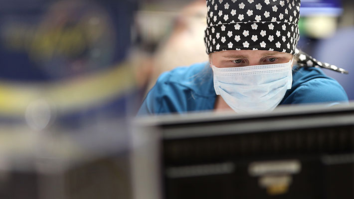 Woman stares at computer with mask on