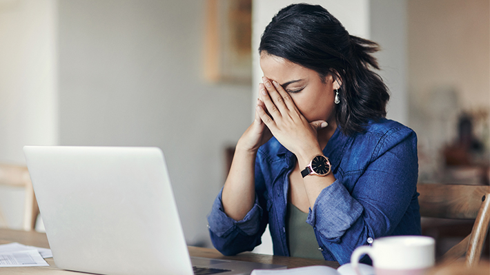 Woman sitting at her laptop with face buried in her hands