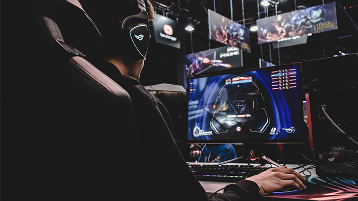 Young man seated at a computer wearing headphones and playing a game