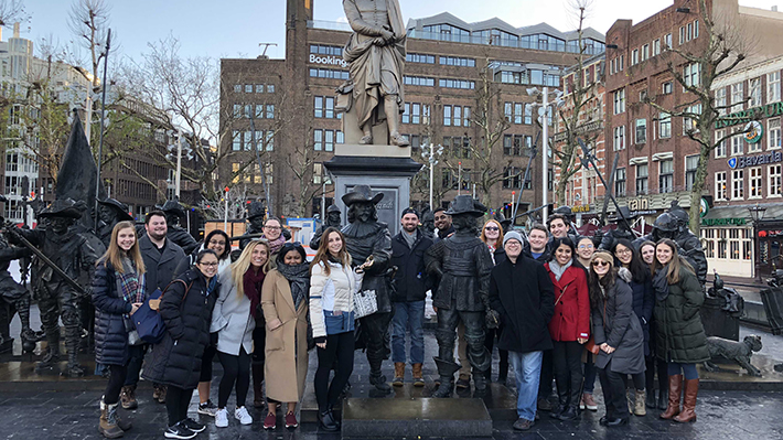 Students gather for a photo in front of a statue in Amsterdam