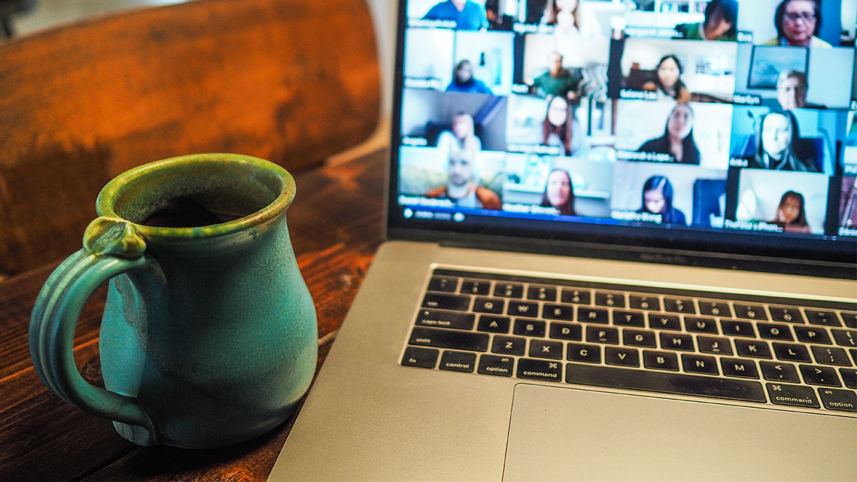 Green coffee cup on left, laptop screen with Zoom discussion visible on right