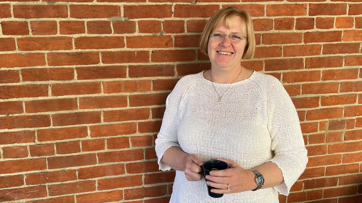 Woman wearing a white sweater holding a coffee cup standing against a brick wall