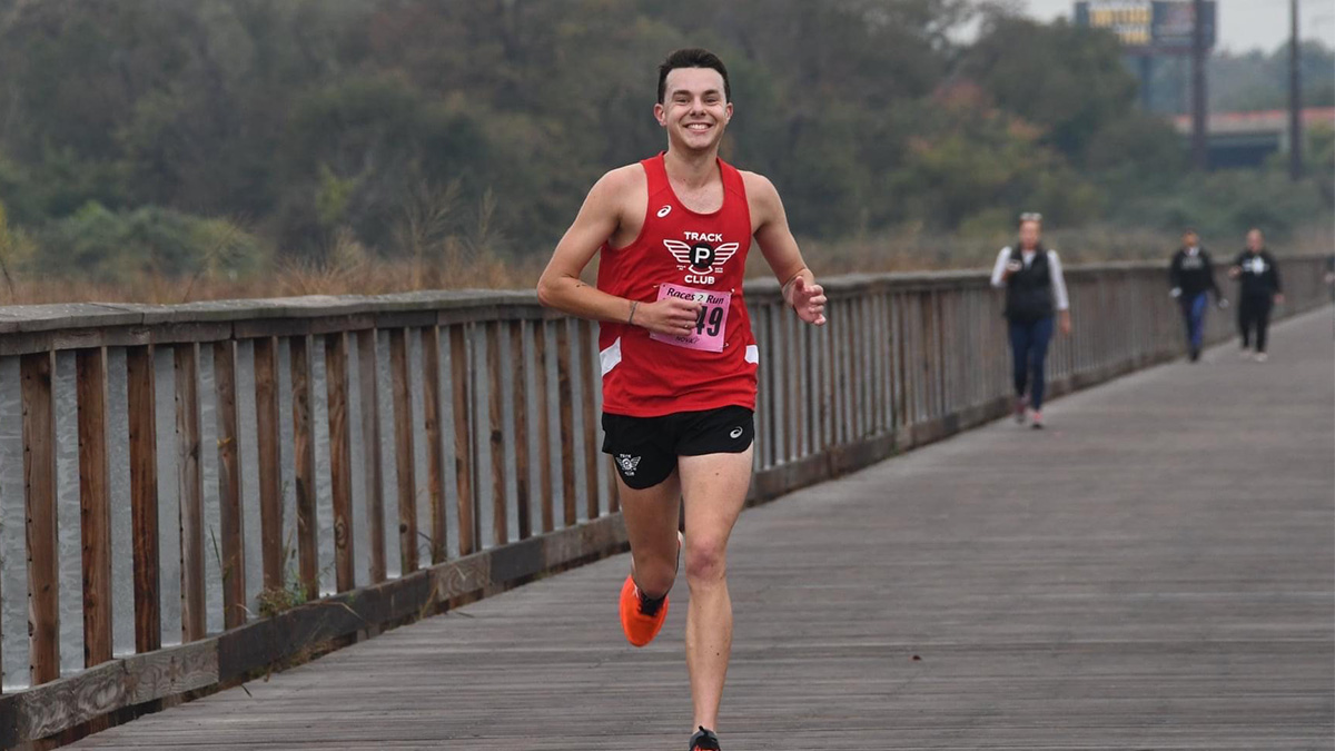 A young man wearing a red tank top, black short and orange shoes running