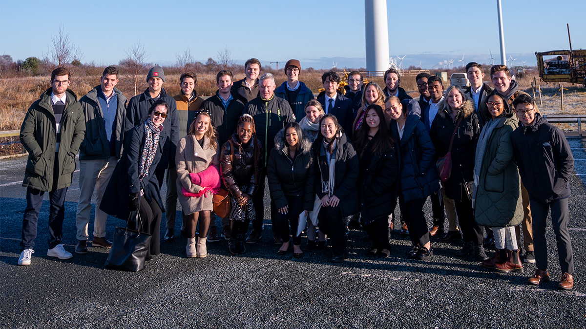 A group of students standing outdoors, with wind turbines visible in the background