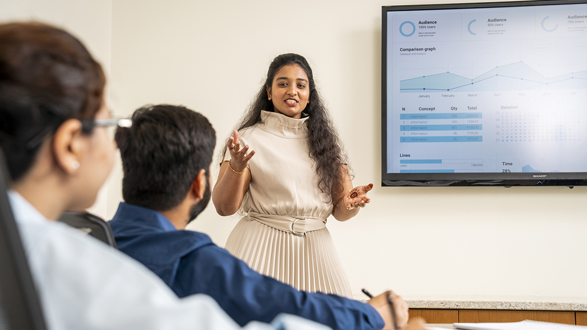 Woman leading a discussion with charts on the screen in the background