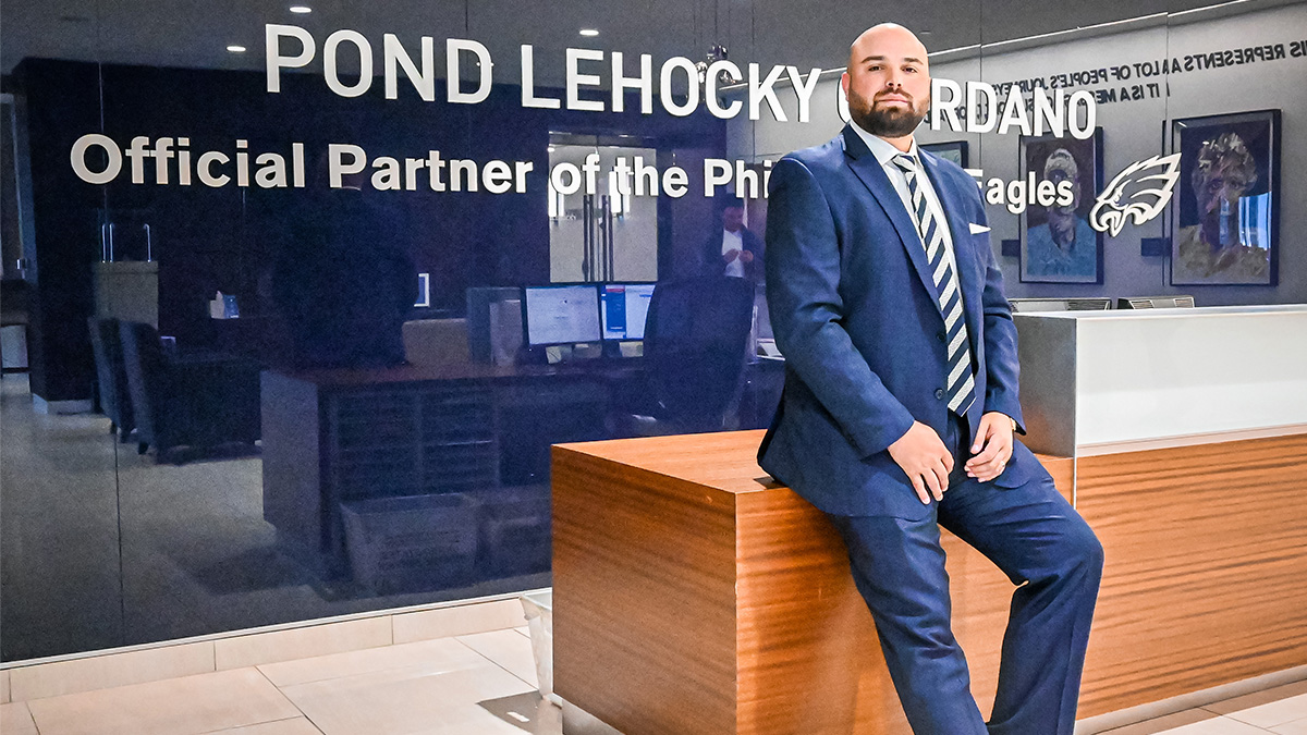 A man in a blue suit seated on top of a long, light brown reception desk