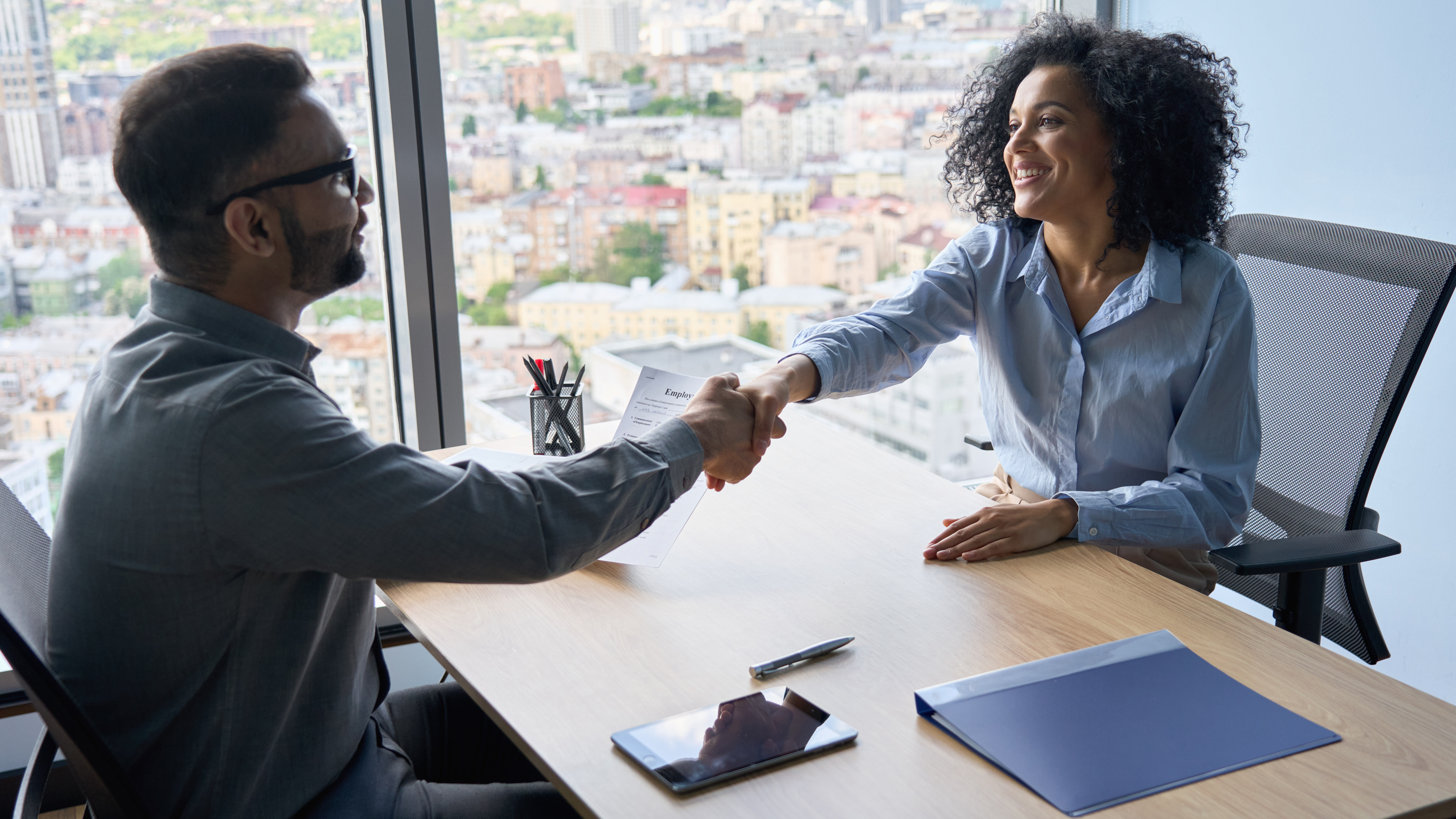 Two people shaking hands sitting at an an office desk