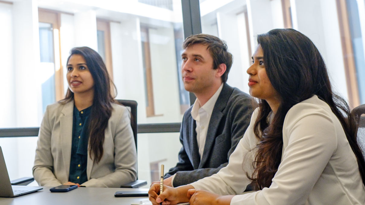 Two female students and one male student in a classroom paying attention to the professor