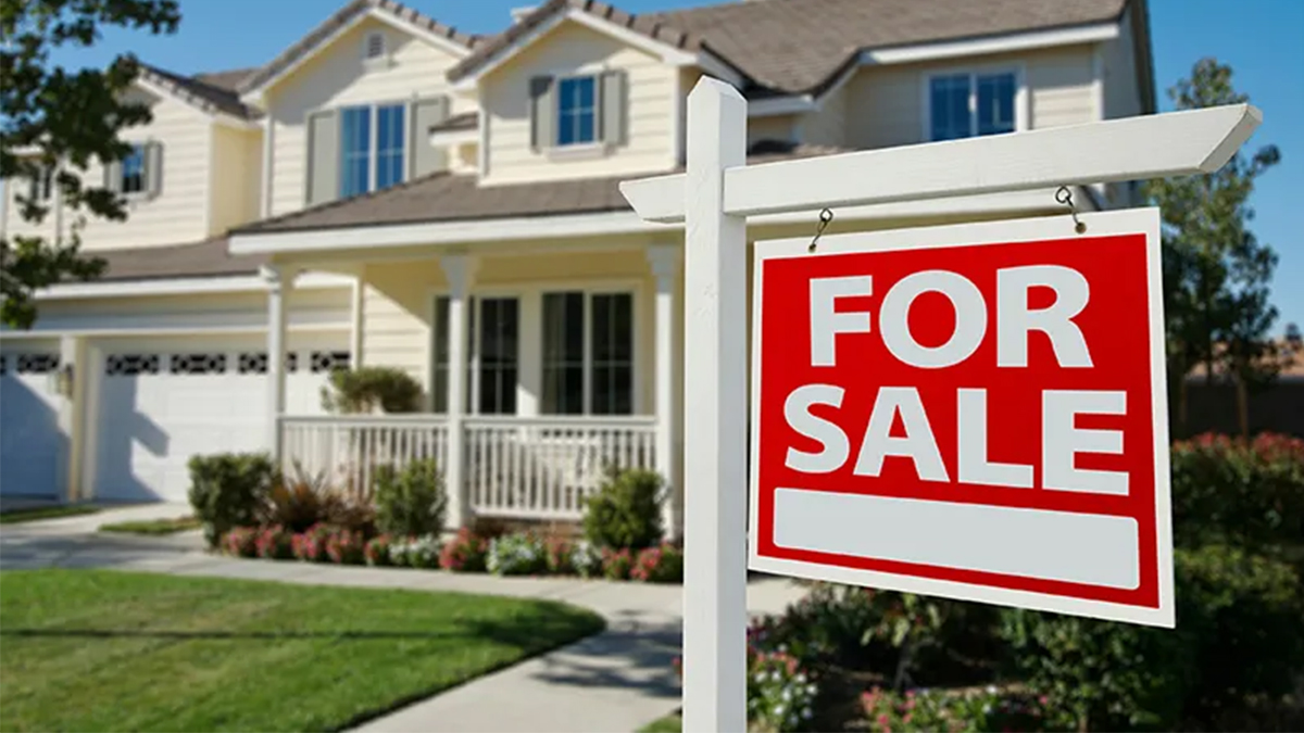 Red and white sign saying For Sale in front of a house