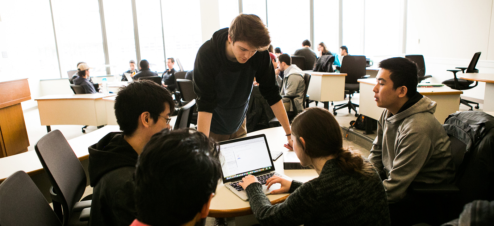 Undergraduate students work collaboratively around a laptop computer in a classroom