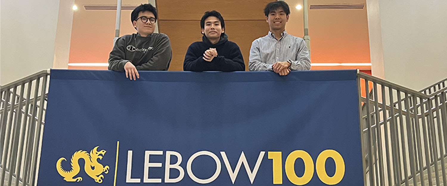 Three young men standing looking over a railing above a banner reading LEBOW 100