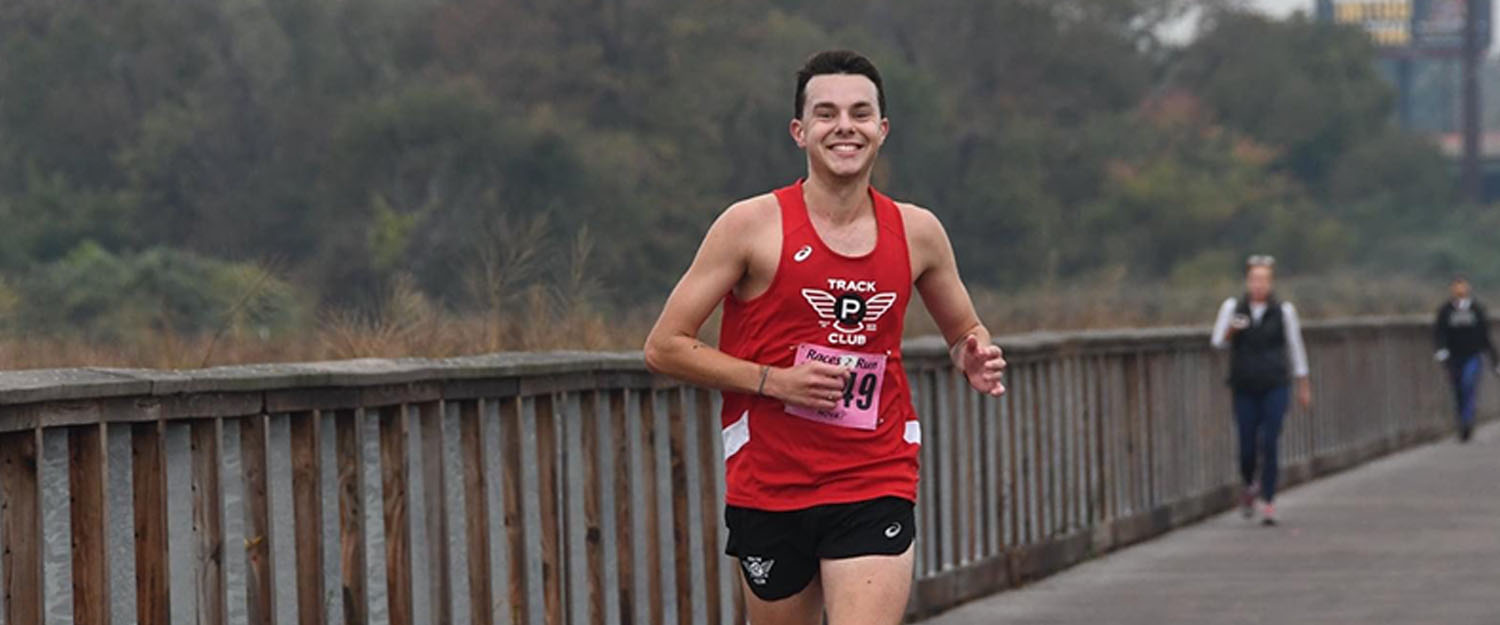 A young man wearing a red tank top, black short and orange shoes running