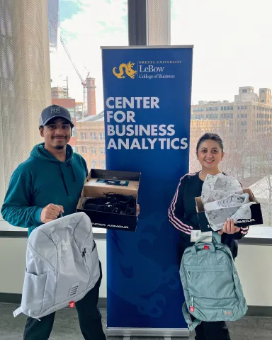 A man and a woman smiling while holding athletic shoes and backpacks