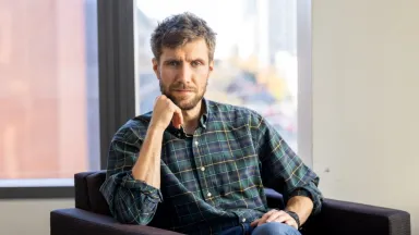 Landscape shot of Tristan Potter, PhD Associate Professor of Economics sitting in chair in front of window