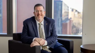 Headshot of Jeffrey Spence, Director of Alumni Relations and Engagement sitting in chair by window