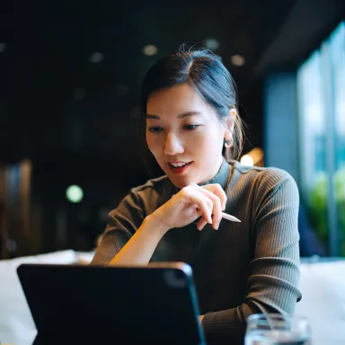 a woman smiles to herself, chin on hand as she works on a laptop