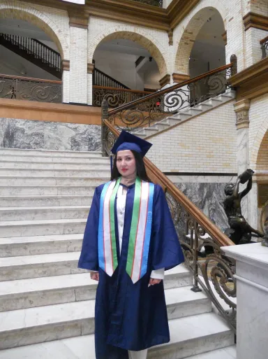 A young woman wearing a graduation cap and gown in the Main Building courtyard at Drexel University