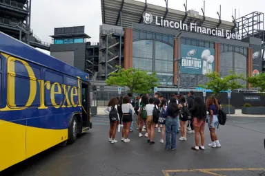 A group of students outside of Lincoln Financial Field with a Drexel-branded bus visible on the left