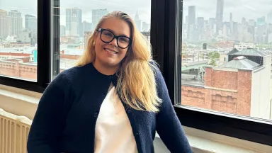 Anette Eilertsen-Dillon smiles while standing by a window holding her laptop.