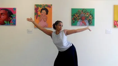 Ari Cabrera poses with arms extended in front of colorful artwork display on a white gallery wall.