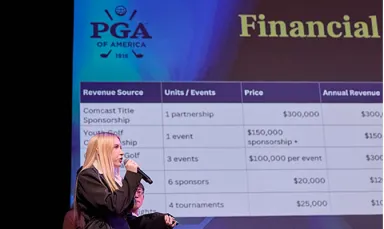 A young woman with blond hair wearing a black shirt and speaking into a microphone with the PGA of Philadelphia logo against a blue backdrop and the word Financial visible on a screen behind her