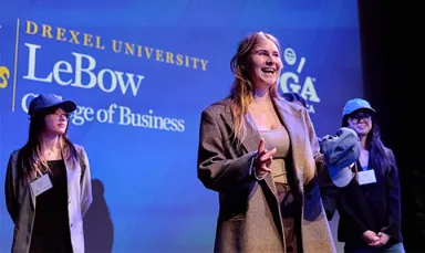 Three young women in business attire standing against a blue backdrop with the LeBow College of Business logo visible and the PGA of Philadelphia logo partly visible