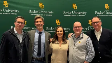 Men and women in business attire standing in front of a green backdrop with the logo for the Baylor University Hankamer School of Business