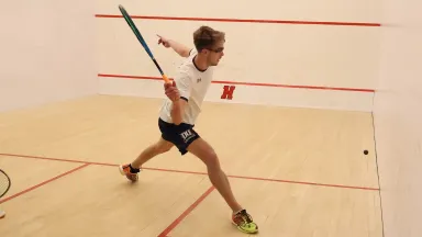 A young man in athletic attire swinging a racket at a squash ball