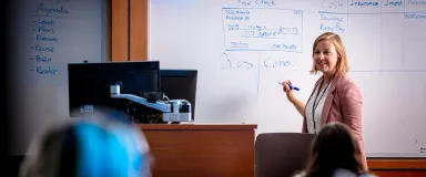 Woman teaching in front of whiteboard with students in foreground.