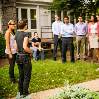 Group of people standing outside a building, listening to a woman.