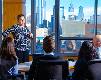 Woman presenting to students from within the LeBow College of Business, Philadelphia's skyline visible through the window.