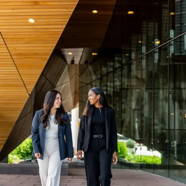 Two women walking and talking outside modern glass building on Drexel's campus..