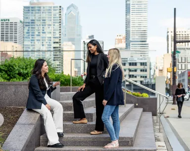 Three Drexel LeBow students in business casual clothing on outdoor concrete steps with Philadelphia's city skyline behind.