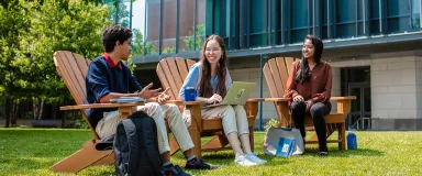 Three students sitting on wooden chairs on Drexel's campus.