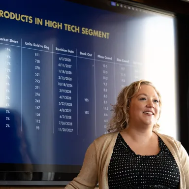 EMBA student standing in front of large screen displaying sales data chart.