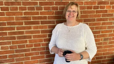 Woman wearing a white sweater holding a coffee cup standing against a brick wall