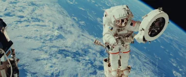 An astronaut with an American flag on his or her space suit during a spacewalk, with the Earth visible in the background