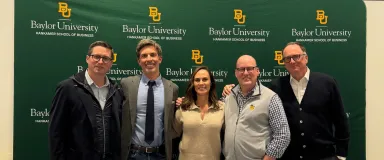 Men and women in business attire standing in front of a green backdrop with the logo for the Baylor University Hankamer School of Business