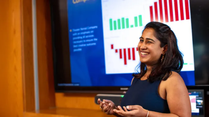 A graduate student making a business presentation in a boardroom with corporate logos visible in the background