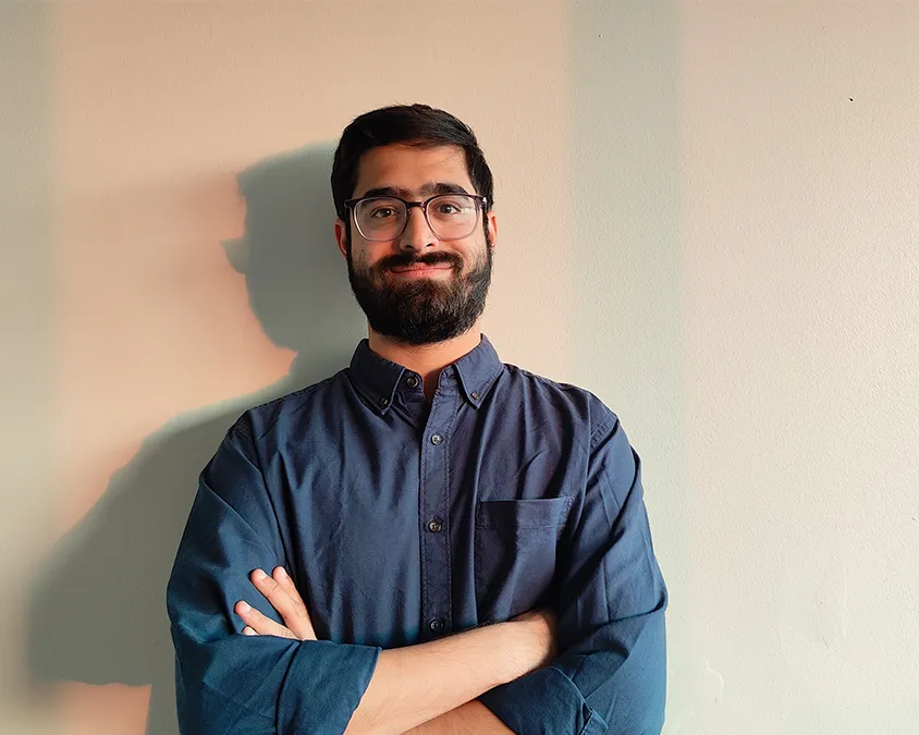 Roshan stands against a light background, smiling with his arms crossed.