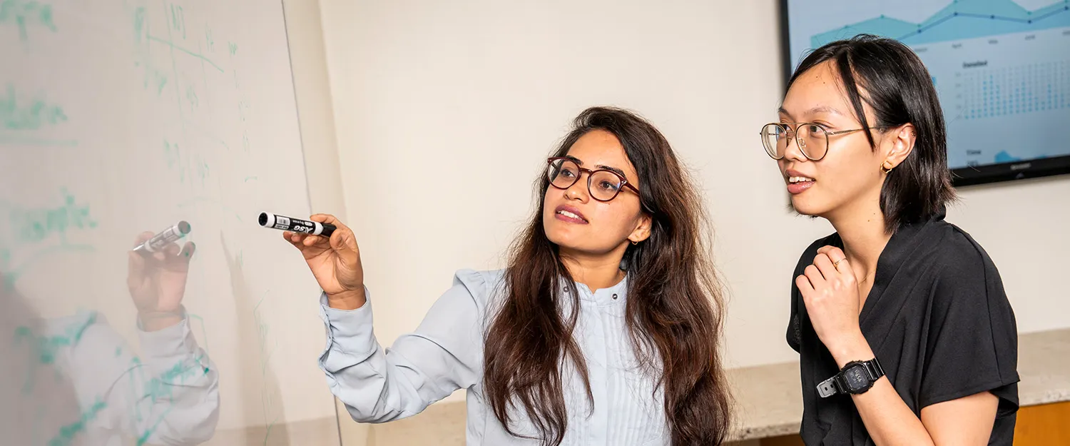 Two students work together at a white board during an economics class.